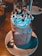 A creamy dessert drink served in a mason jar, topped with whipped cream, chocolate sauce, and colorful sprinkles. The drink is placed on a round white plate with a metal straw and a spoon beside it.