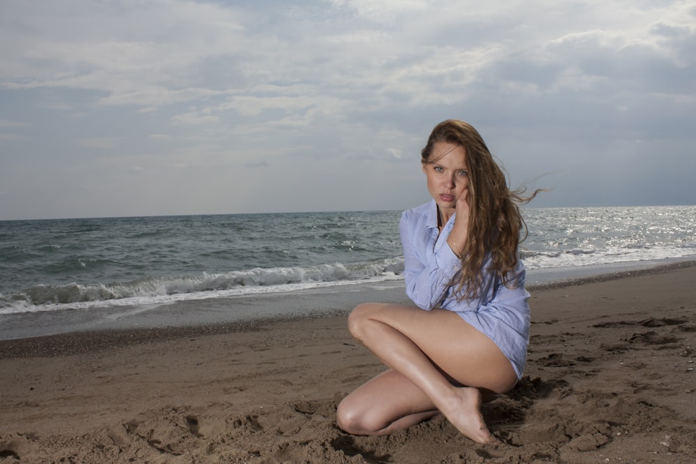 woman in white dress shirt sitting on beach during daytime