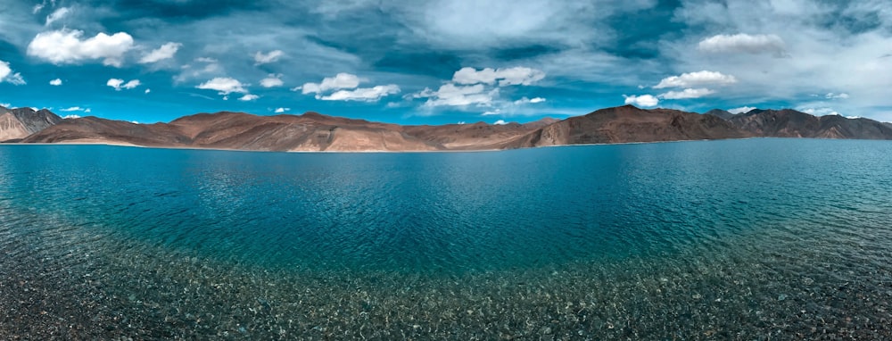 brown mountain near body of water under blue sky during daytime