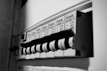 A close-up view of an electrical circuit breaker panel featuring multiple labeled toggle switches. Each switch has labels with details such as voltage and circuit specifications. The panel is monochrome, highlighting the structural design and text.