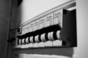 A close-up view of an electrical circuit breaker panel featuring multiple labeled toggle switches. Each switch has labels with details such as voltage and circuit specifications. The panel is monochrome, highlighting the structural design and text.