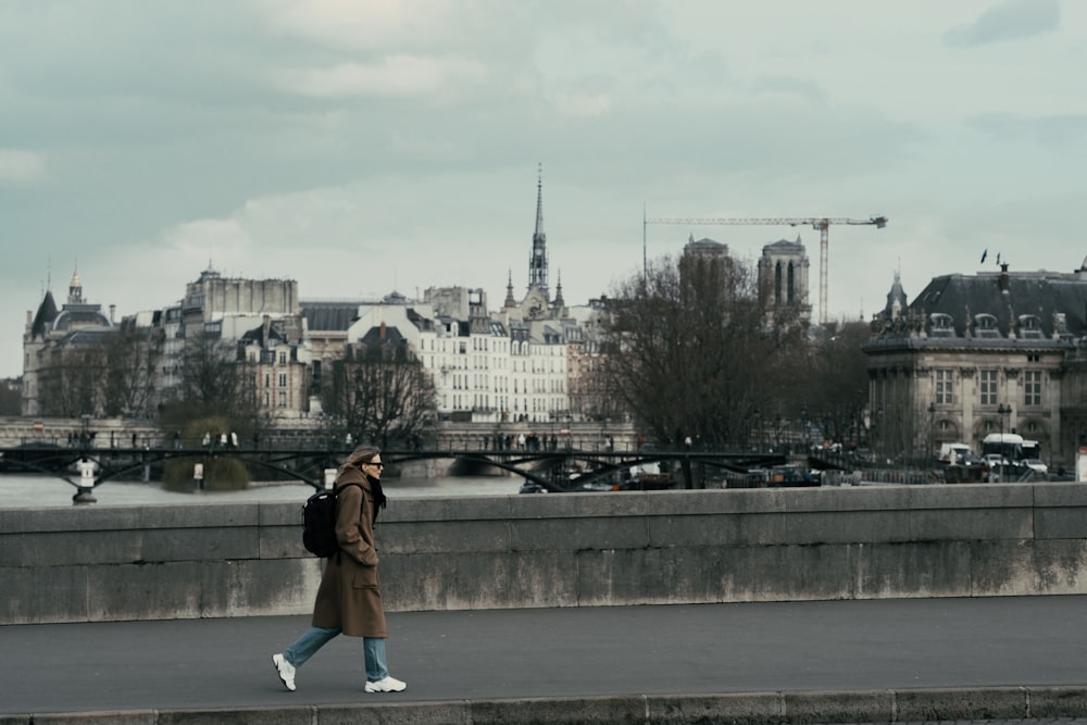 woman in brown jacket and blue denim jeans sitting on white chair looking at city buildings