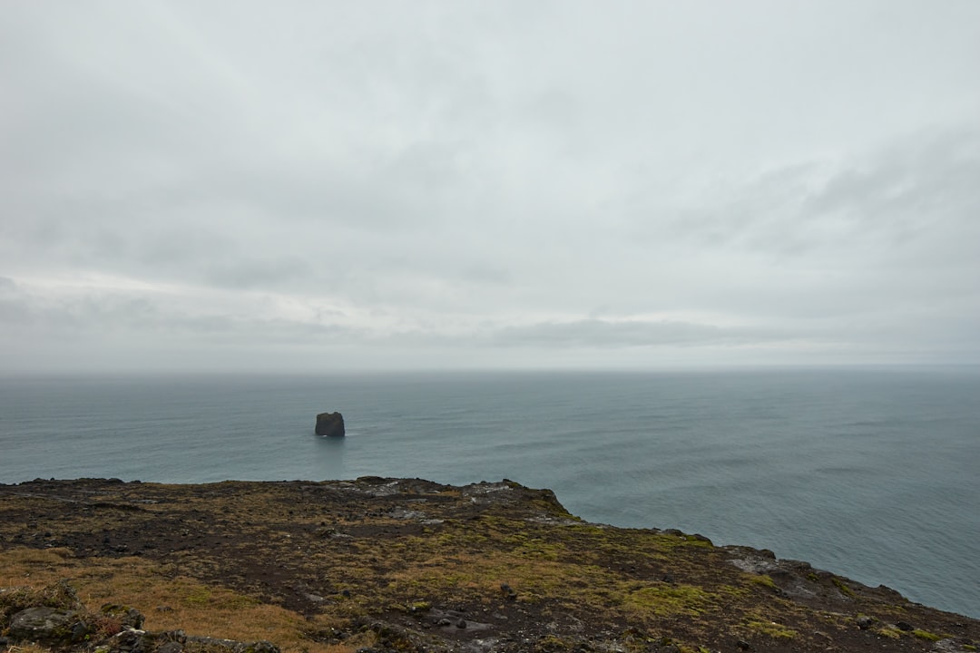 person standing on cliff near sea under cloudy sky during daytime