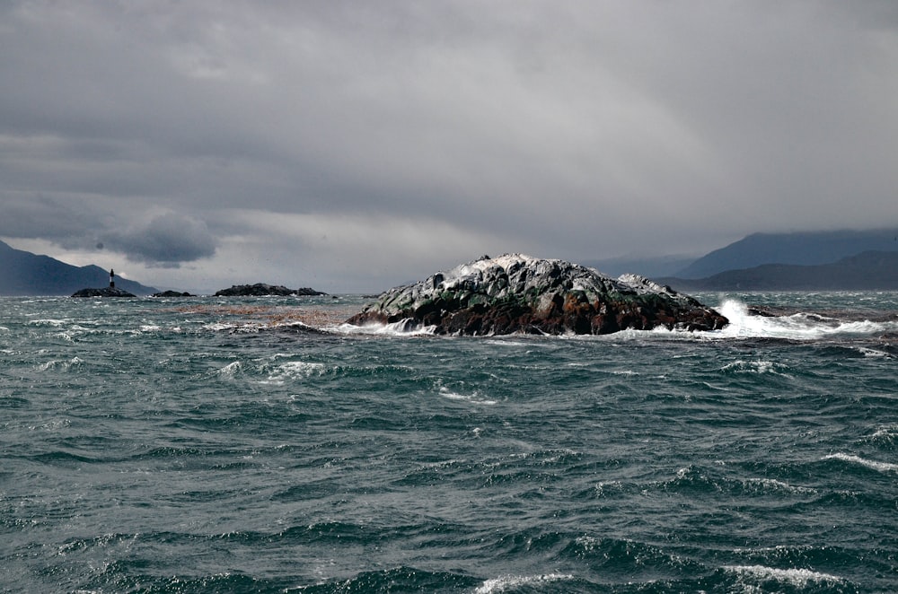 brown and black rock formation on sea under gray clouds