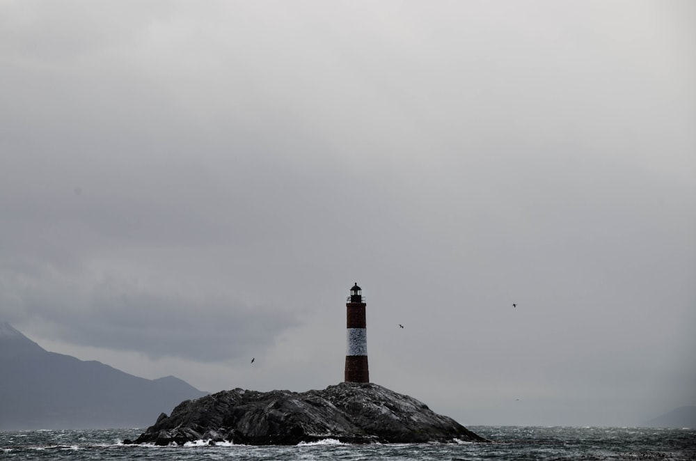 brown and white lighthouse on black rock formation under white clouds during daytime