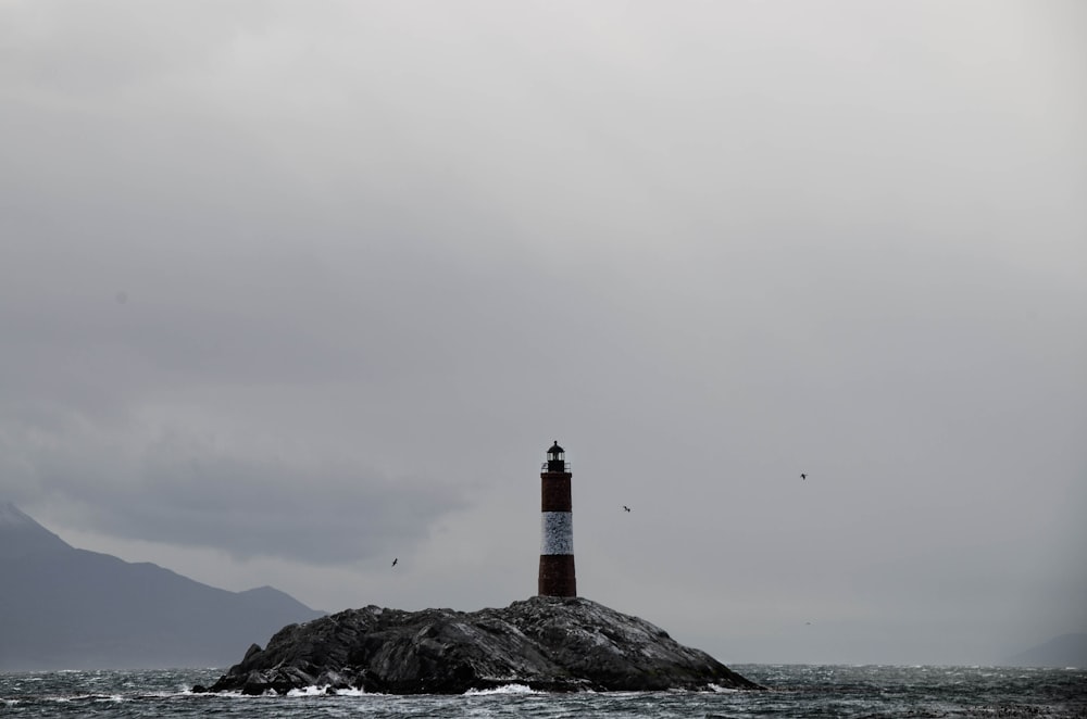 Faro marrone e bianco sulla formazione rocciosa nera sotto nuvole bianche durante il giorno