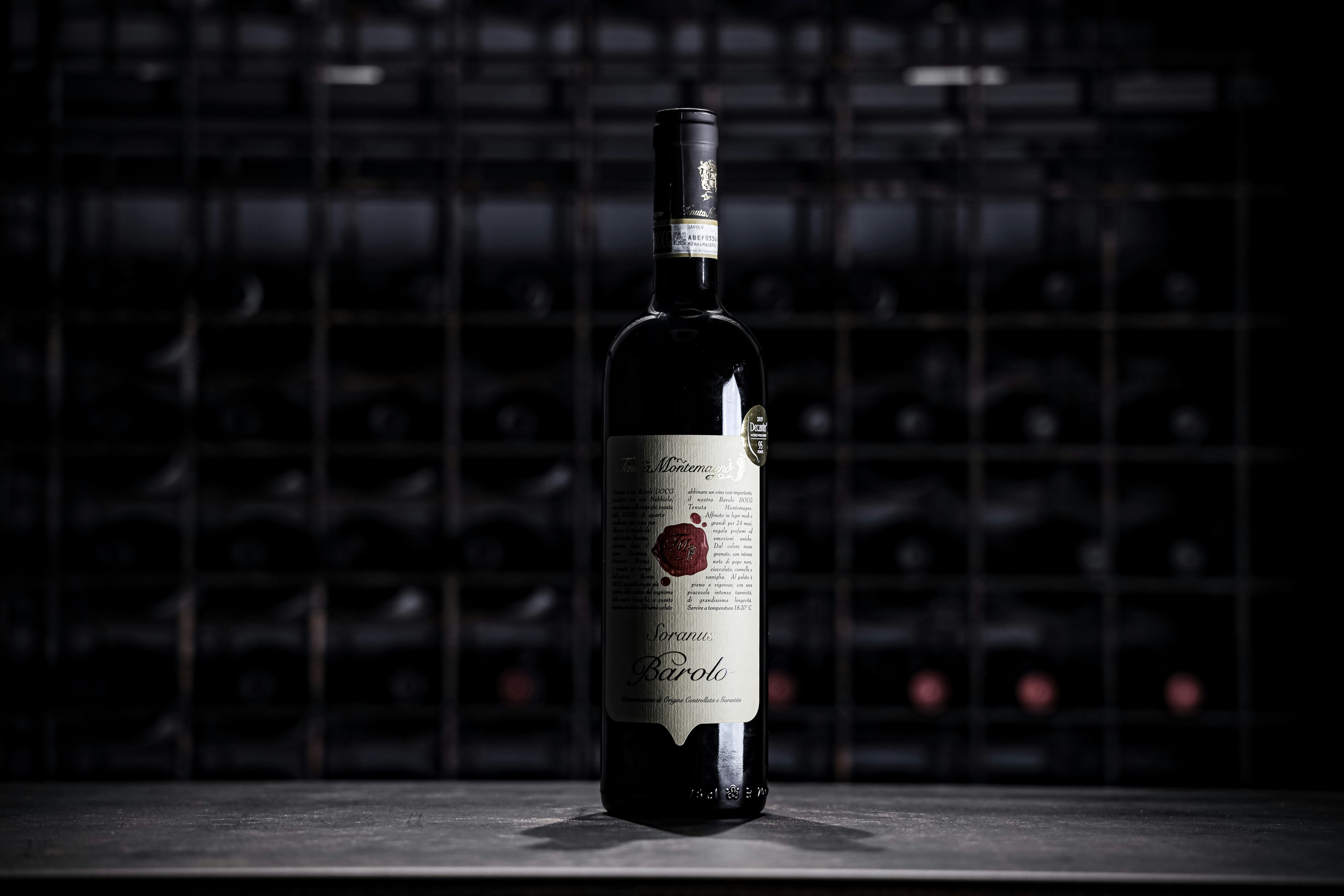 Deep garnet Barolo wine in large Burgundy glass, warm amber side light, stone cellar background