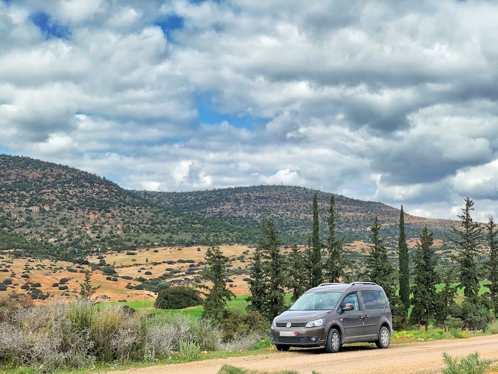 silver suv on road near green trees under white clouds and blue sky during daytime