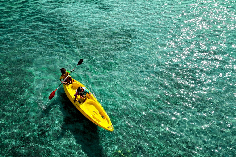 Person, die tagsüber gelbes Kajak auf grünem Meer fährt
