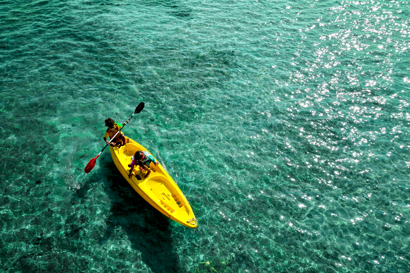 A yellow kayak seen from above on clear turquoise water near the shore