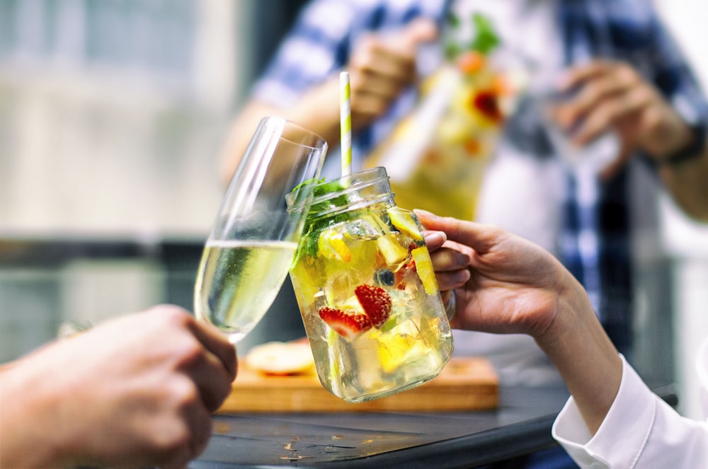 person holding clear drinking glass with yellow liquid