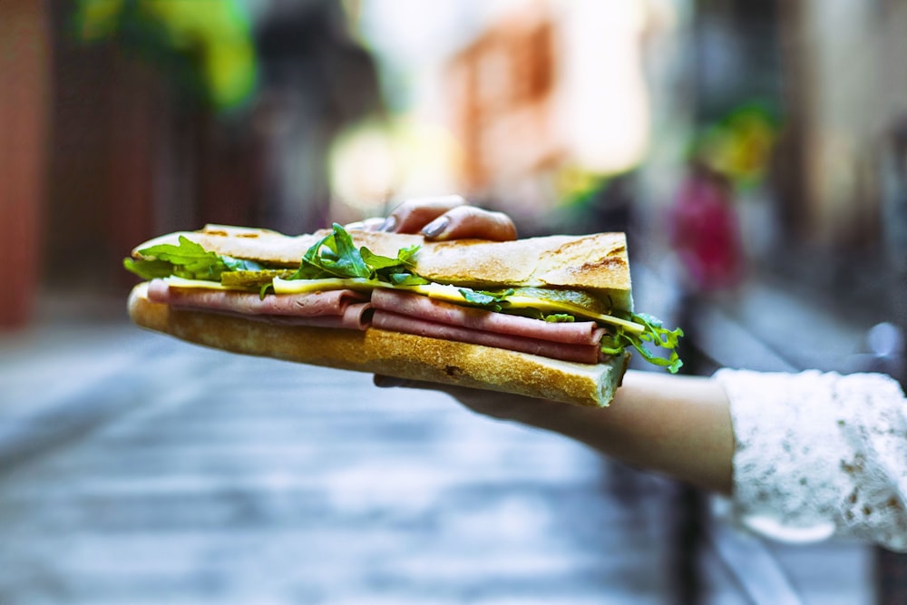 person holding brown bread with green leaf vegetable