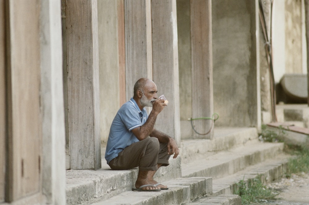 uomo in camicia blu e pantaloni marroni seduto sulla panchina di cemento durante il giorno