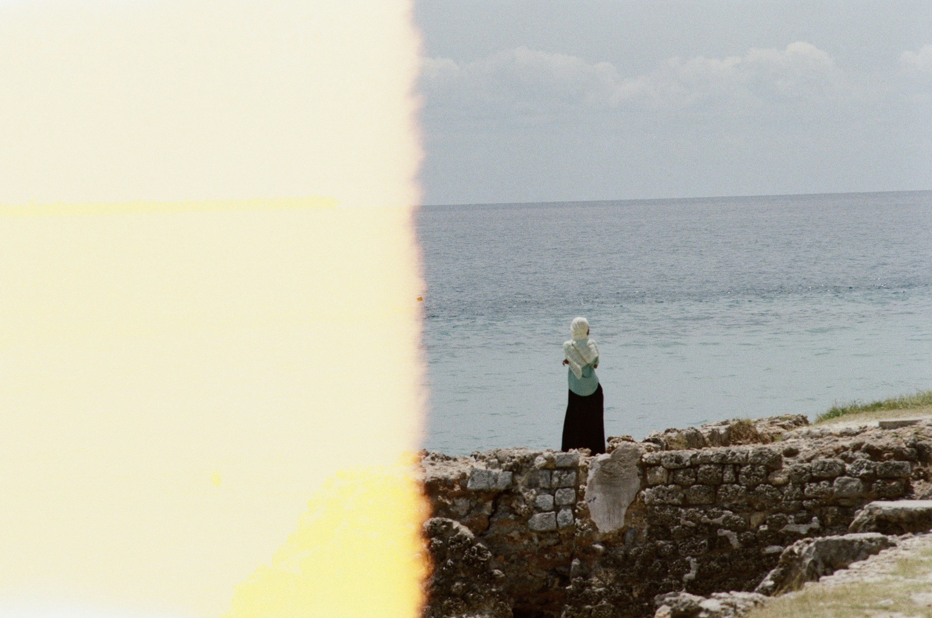 woman in green jacket standing on rock near sea during daytime