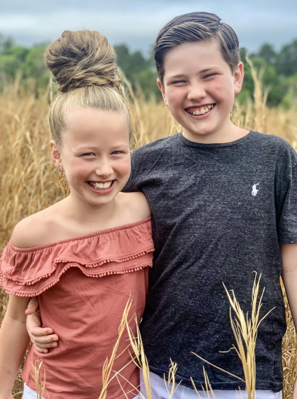 2 girls in red and gray shirts standing on brown grass field during daytime