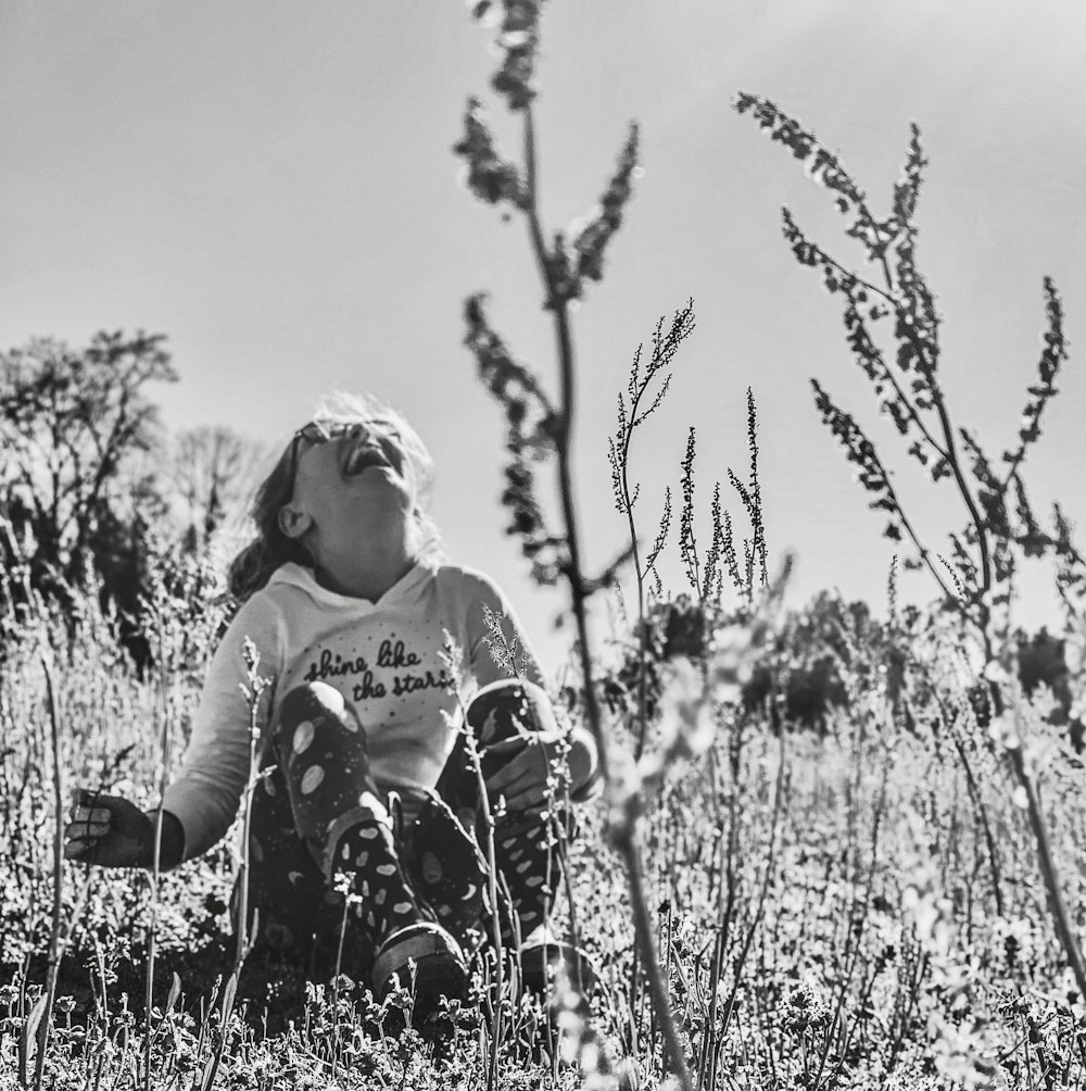 grayscale photo of woman in black and white floral long sleeve shirt standing on grass field
