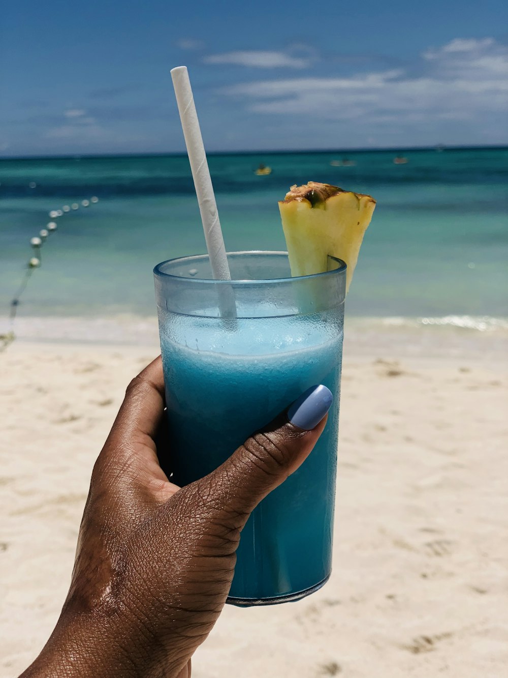 person holding blue liquid in clear drinking glass with white straw