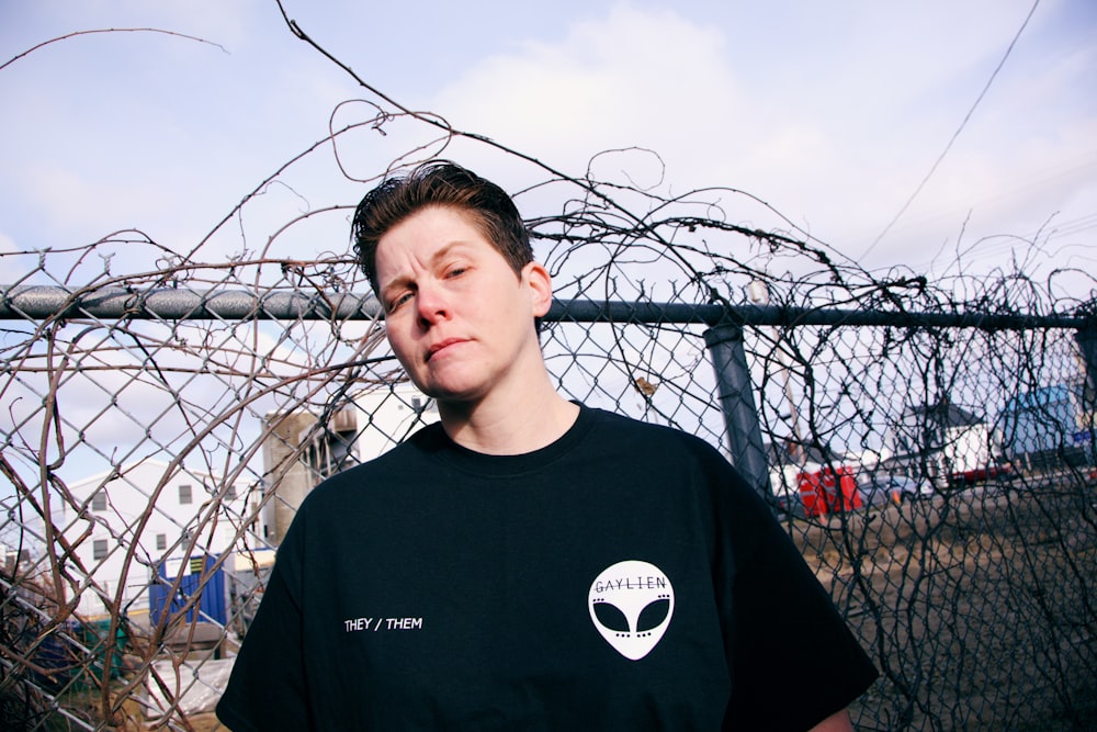 man in black crew neck t-shirt standing near gray metal fence during daytime