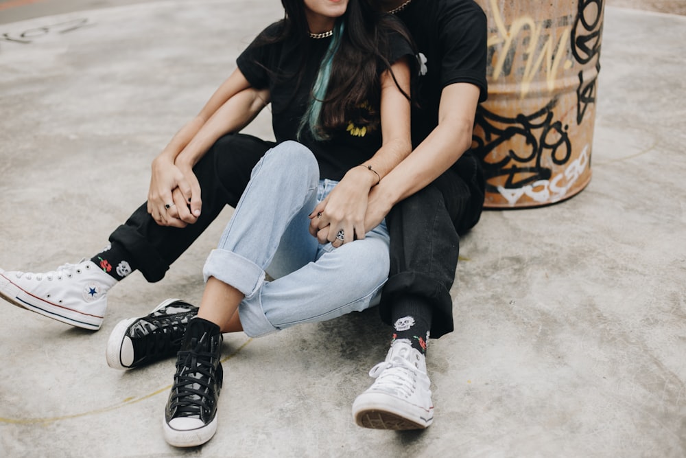 mulher na camiseta preta e jeans azuis sentados no chão de concreto