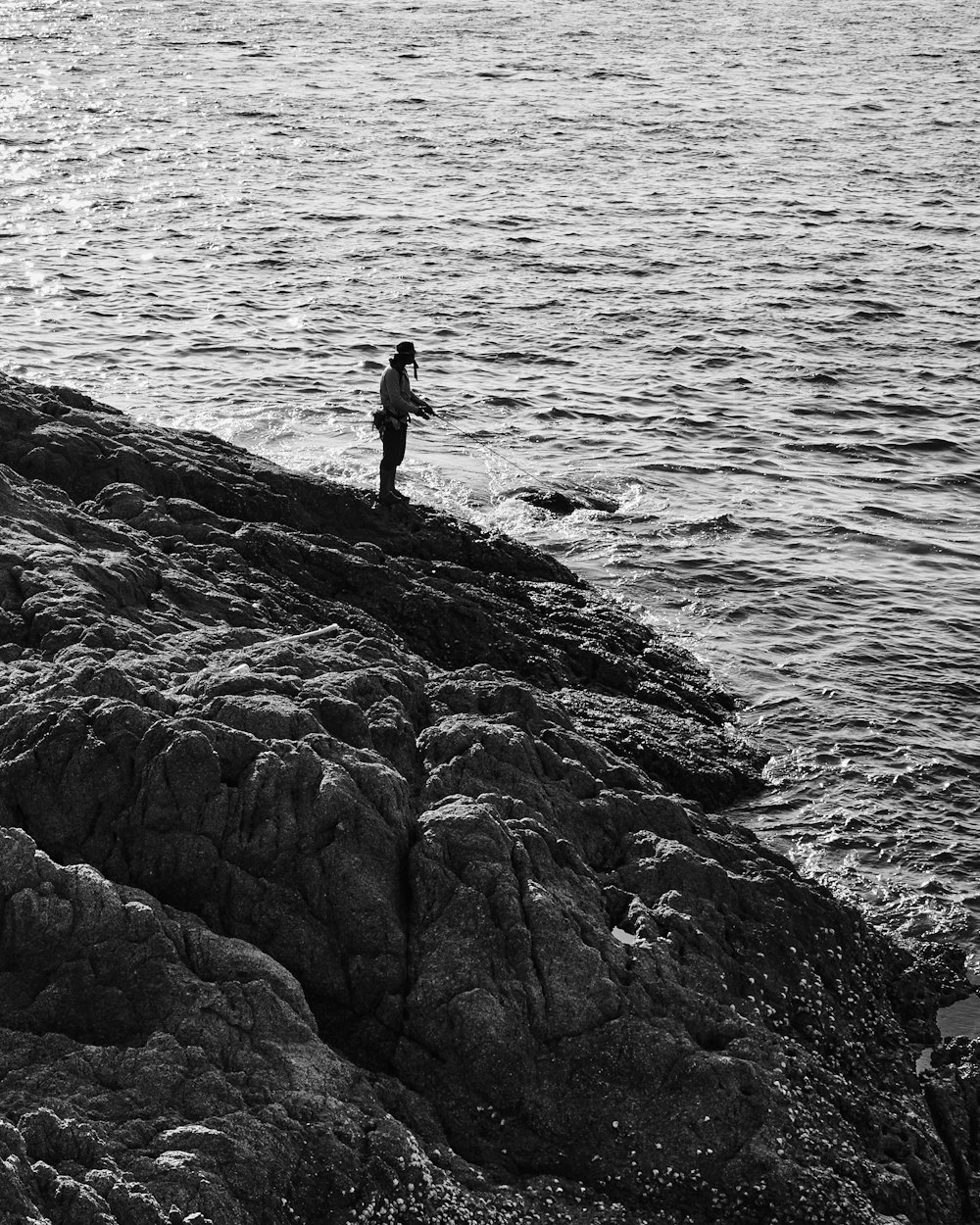 Silhouette d’une personne debout sur une formation rocheuse près d’un plan d’eau pendant la journée