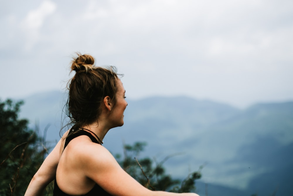 Mujer con camiseta negra sin mangas mirando las montañas durante el día