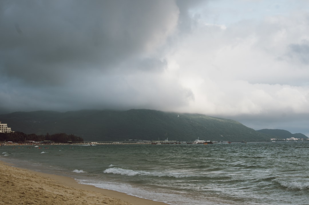 people surfing on sea near mountain under white clouds during daytime