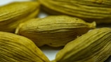 Several dried cardamom pods with a textured, ribbed surface in a light brownish-green color. They are closely arranged, capturing the intricate details of their natural form.
