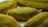 Several dried cardamom pods with a textured, ribbed surface in a light brownish-green color. They are closely arranged, capturing the intricate details of their natural form.
