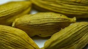 Several dried cardamom pods with a textured, ribbed surface in a light brownish-green color. They are closely arranged, capturing the intricate details of their natural form.