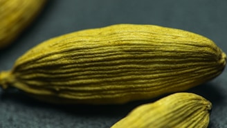 A close-up image of green cardamom pods displaying their elongated, ribbed texture against a dark background.
