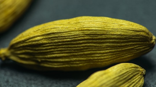 A close-up image of green cardamom pods displaying their elongated, ribbed texture against a dark background.