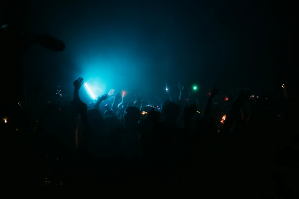 Crowd shot showing hands in the air, neon green and electric blue lights casting dynamic shadows.