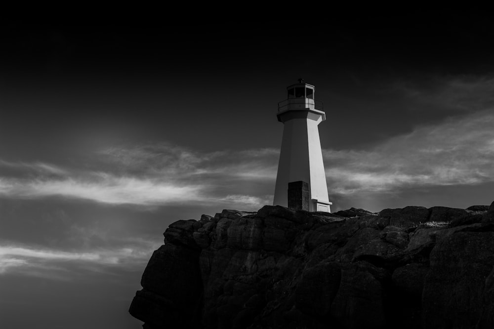 grayscale photo of lighthouse on rock formation