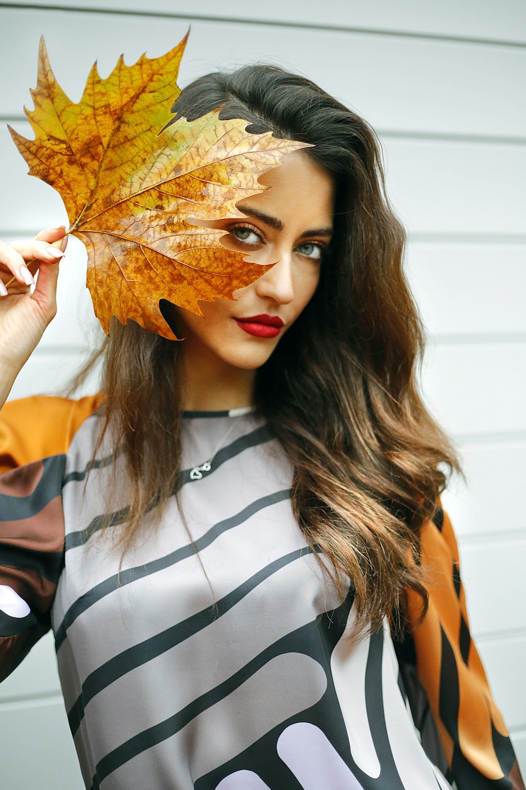 woman in white and black stripe shirt covering her face with brown maple leaf