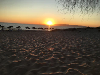 A serene beach scene at sunset with elegant summer accessories artfully arranged on soft sand.