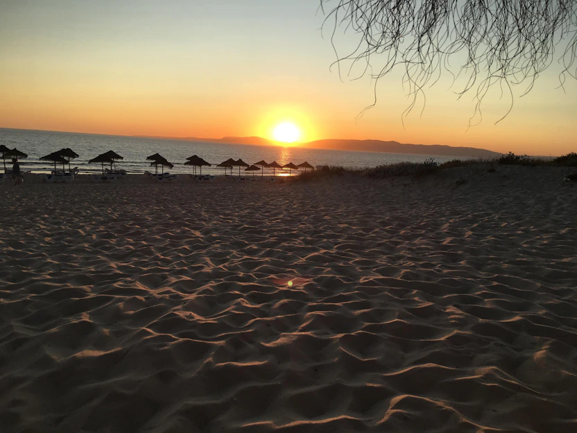 A serene beach scene at sunset with elegant summer accessories artfully arranged on soft sand.