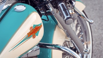 Close-up view of a motorcycle featuring intricate chrome details and a prominent gas tank with a Harley-Davidson logo. The turquoise and cream-colored paint adds a vintage aesthetic, complemented by shiny metallic elements.