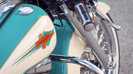 Close-up view of a motorcycle featuring intricate chrome details and a prominent gas tank with a Harley-Davidson logo. The turquoise and cream-colored paint adds a vintage aesthetic, complemented by shiny metallic elements.