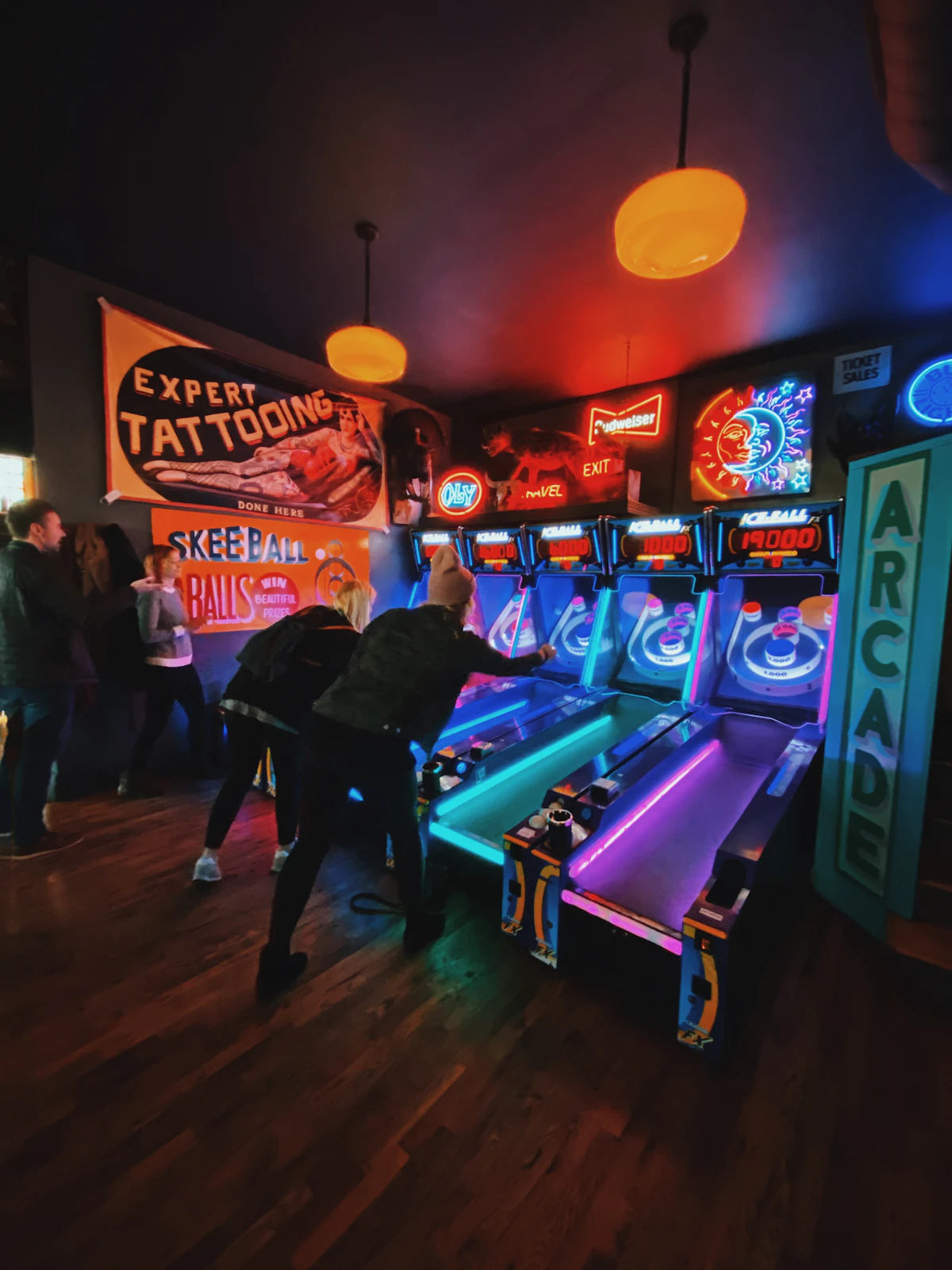 Friends playing Skee-Ball and retro games inside a glowing neon arcade