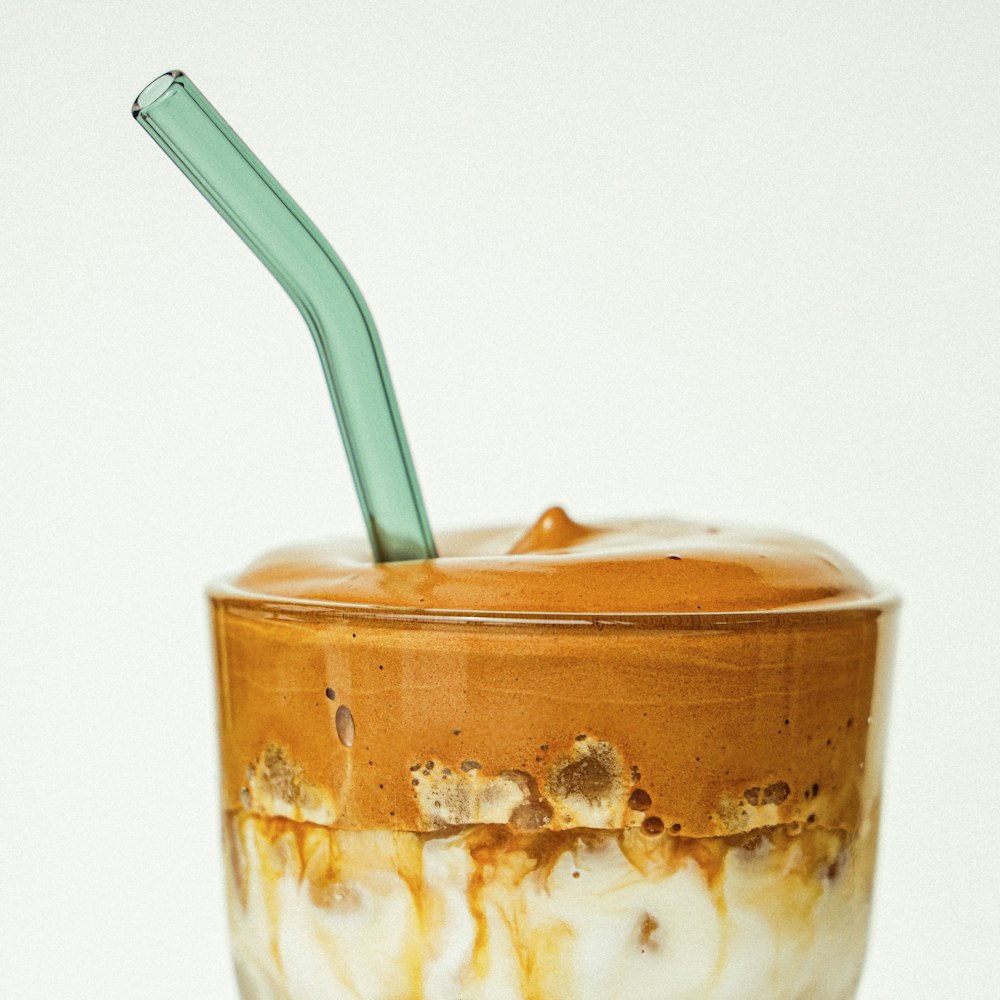 clear drinking glass with brown liquid and green straw