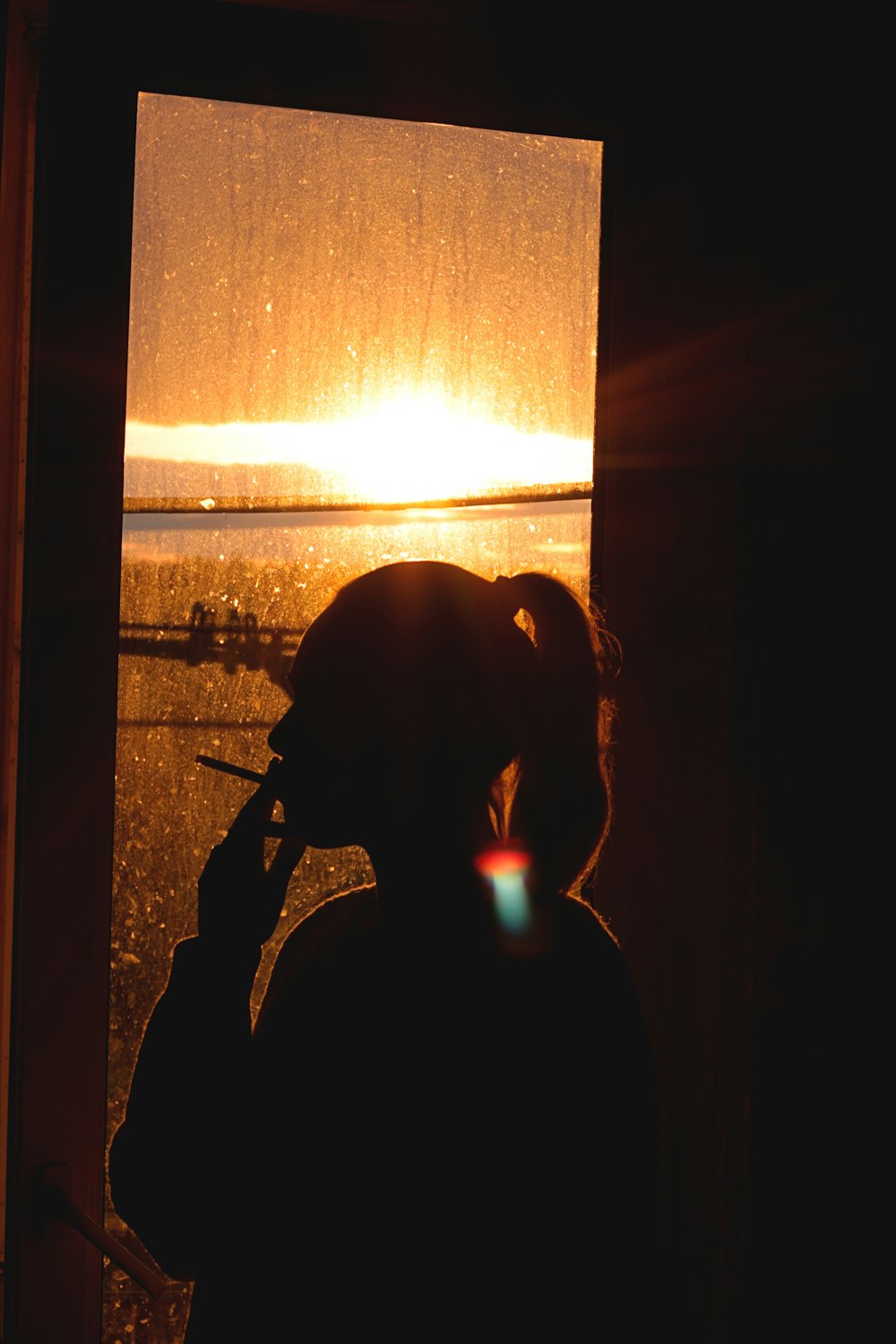 silhouette of woman standing near window during sunset