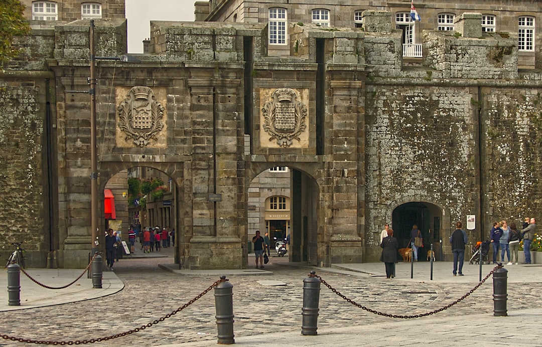 people walking on sidewalk near building during daytime, La Porte Saint-Vincent a été construite en 1708. Elle porte le nom du diacre martyrisé en Espagne au IV siècle.<p></figure>Deux écussons apparaissent sur la façade celui de droite symbolise le Duché de Bretagne celui de gauche arbore les armoiries de la ville : la herse surmontée de l’hermine des ducs de Bretagne.