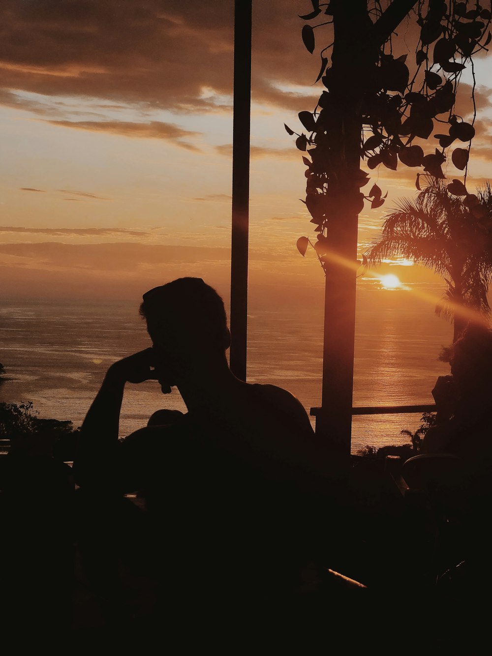 silhouette of woman sitting on rock near body of water during sunset