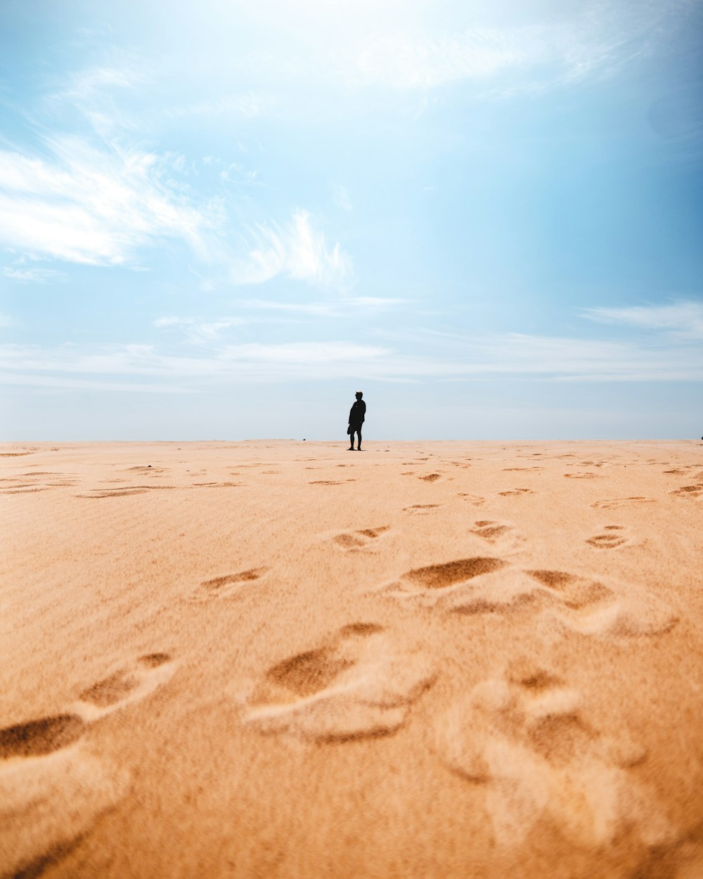 person in black jacket walking on brown sand under blue sky during daytime