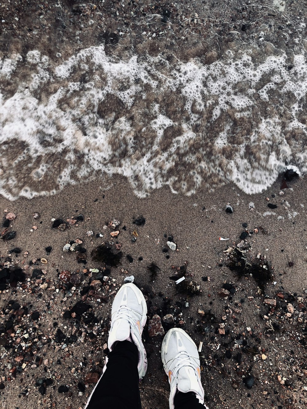 Persona con zapatillas blancas de pie sobre arena marrón