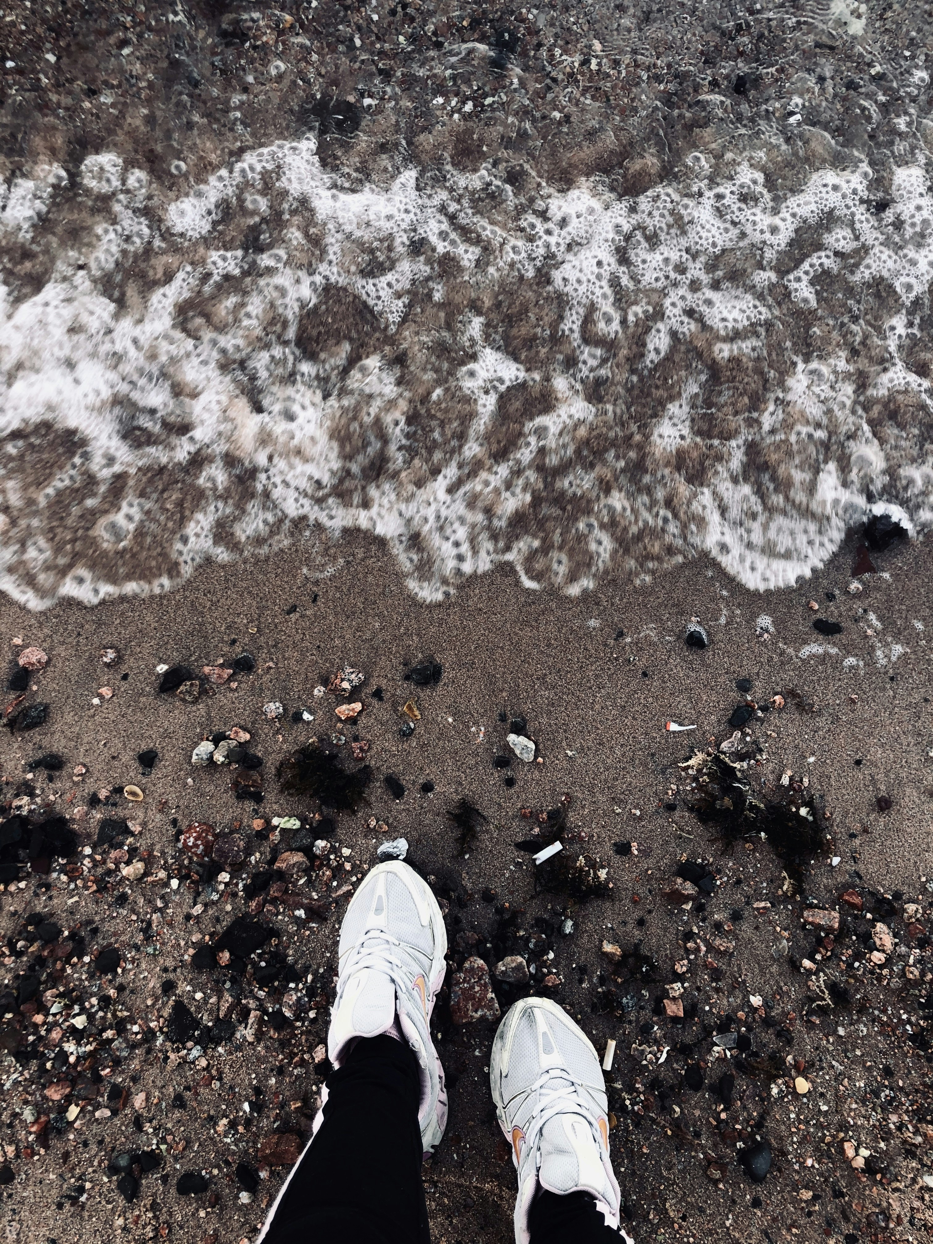 person in white sneakers standing on brown sand