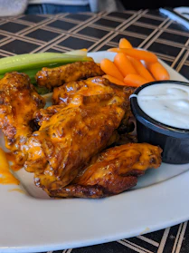 Close-up of crispy golden wings glazed with spicy sauce, served with a side of fresh celery sticks.