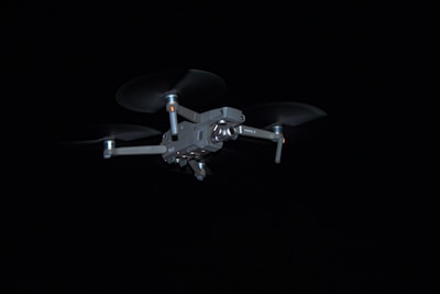 A sleek black drone hovering smoothly against a dark sky background.