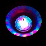 A vibrant, colorful light display featuring a central crystal-like structure surrounded by a radiant halo of multicolored lights, creating a mesmerizing effect against a dark background.