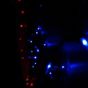 A string of bright blue LED lights arranged in a pattern, with smaller red lights forming a line to the left. The scene is dark, emphasizing the vivid glow of the lights against the shadowy background.